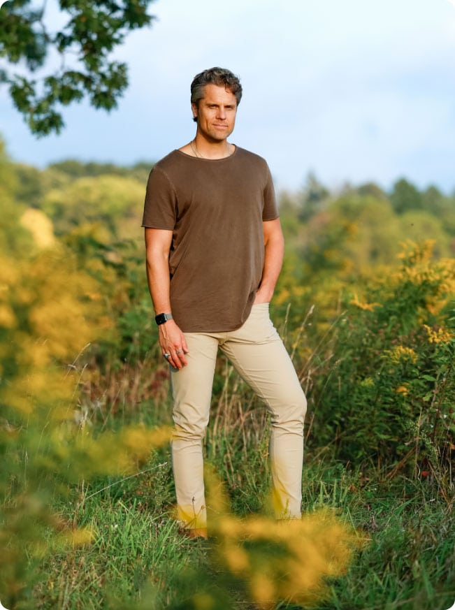 A confident spiritual coach standing outdoors in a lush green field, promoting mindfulness and personal growth through coaching and meditation practices.