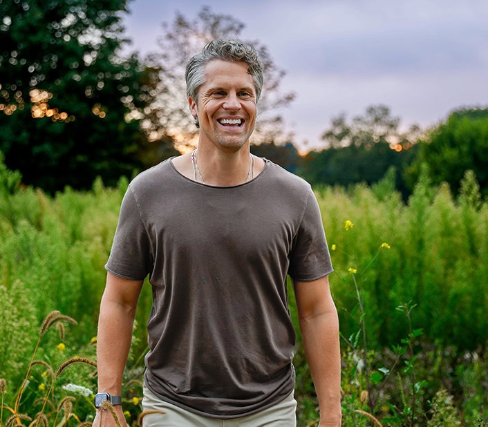 Ben Katt, spiritual coach and meditation teacher, smiling outdoors in a lush green field during sunset, promoting mindfulness and inner peace.